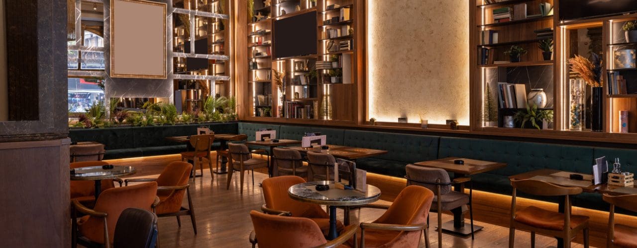 Warm restaurant interior with flexible seating, timber shelving, ambient lighting and planted banquettes designed for comfortable dining.