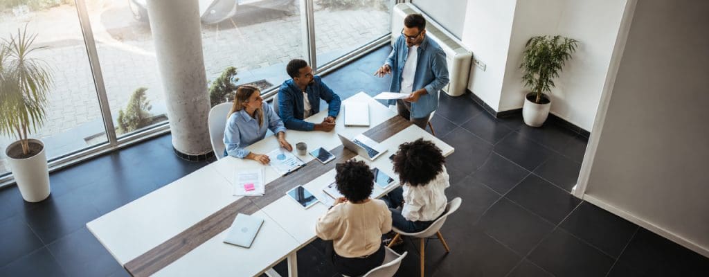 Team collaborating around a conference table in a modern office, reviewing documents, laptops and project plans during a strategy meeting.