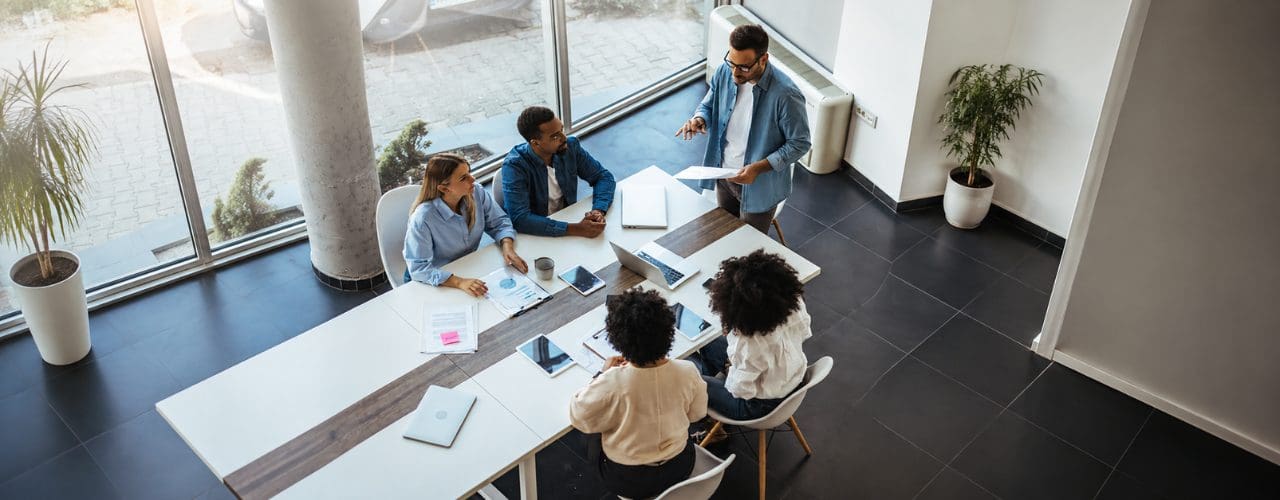 Team collaborating around a conference table in a modern office, reviewing documents, laptops and project plans during a strategy meeting.