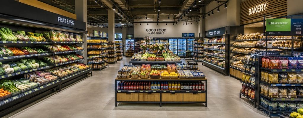 Modern supermarket interior with clearly defined fruit and veg, bakery and food-to-go zones, organised displays and wide customer pathways.